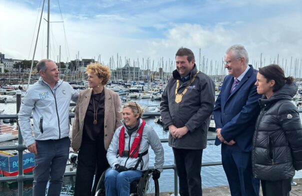 A group of six people with a harbour in the background under a blue sky. They are representatives of the partners delivering BoatHub, an accessible boating service.