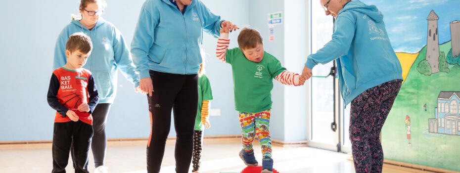 Staff members helping kids across balance obstacle course