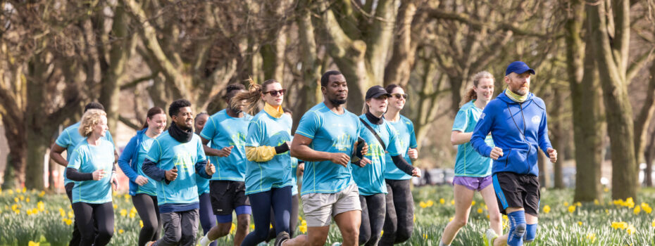 A group of people wearing Sanctuary Runners T-shirts run together through a park.