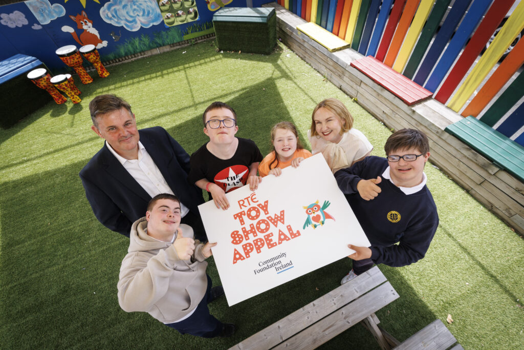 Six people shot from above as they hold an RTÉ Toy Show Appeal logo towards the camera. Kevin Bakhurst of RTÉ (second from left) and Moninne Griffith of Community Foundation Ireland (second from right) are joined by boys and girls of Down Syndrome Centre.