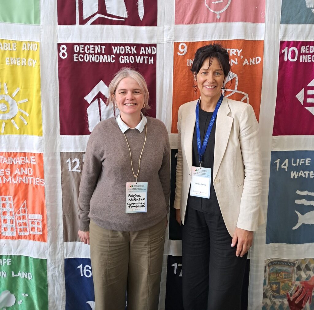 Two women facing the camera with name badges hanging around their necks. The backdrop is a large banner of the United Nation's SDGs. Ailbhe of Community Foundation Ireland is meeting Deirdre Garvey of Atlantic Technology University (ATU), Mayo.