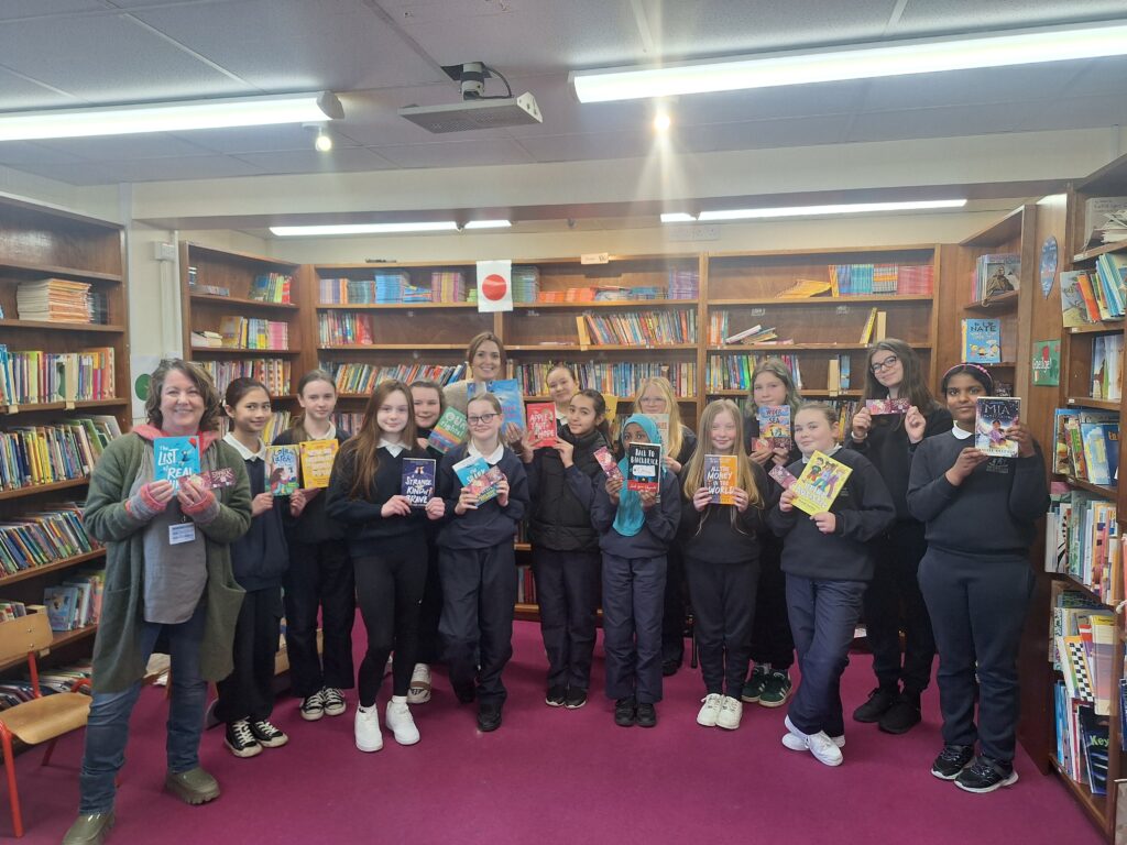 A class photo of children holding books against a backdrop of school library shelves.