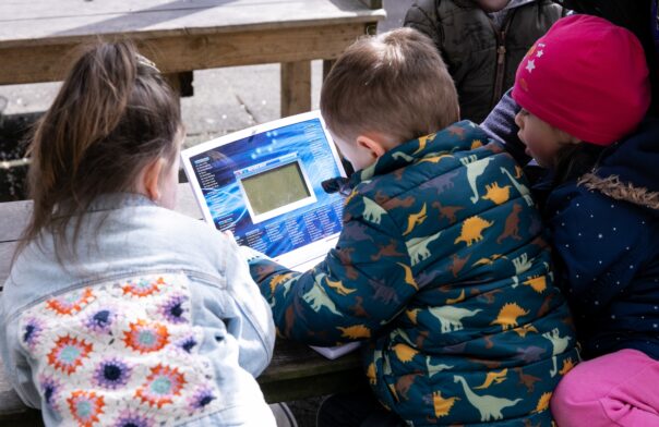 A group of three children playing with an electronic toy with their backs to the camera. The children attend a project by a partner of Community Foundation Ireland.