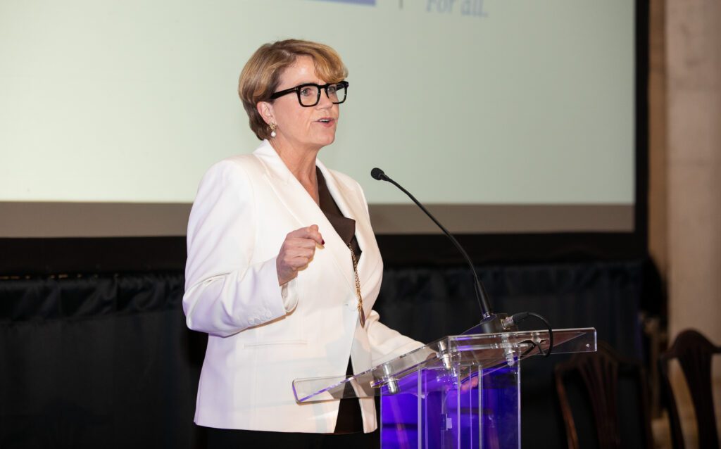 A woman in business attire with a white jacket is standing at a podium delivering remarks. It is Denise Charlton, Chief Executive of Community Foundation Ireland