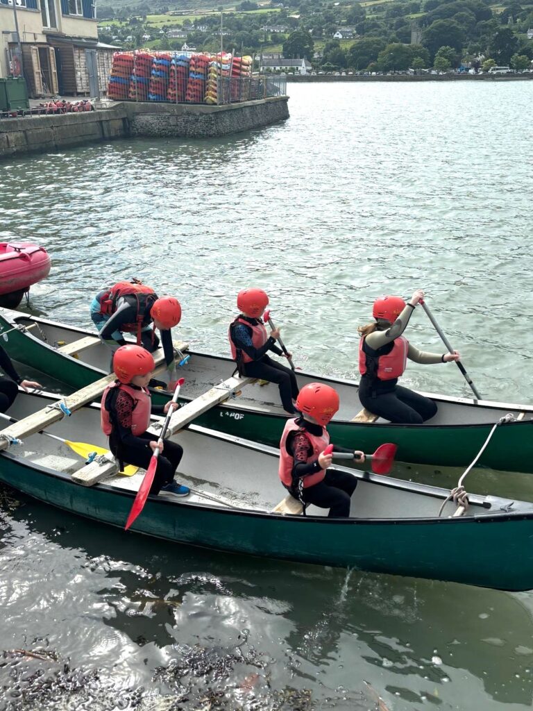 A group of children in two rowing boats about to set off from quayside in Carlingford, Ireland. They are wearing bright orange safety gear.