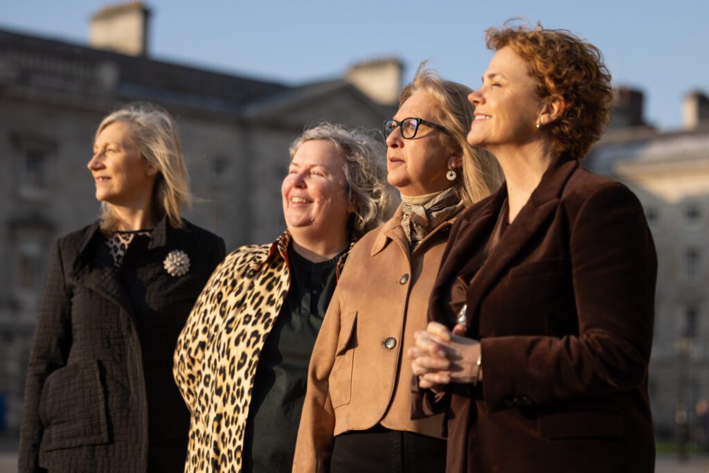 Four women looking towards the sun - which is illuminated their fronts. Against a backdrop of older buildings, in the courtyard of Trinity College Dublin. They are Kate Bond, Chief Advancement Officer, Trinity Development Alumni; Linda Doyle, Provost, Trinity College Dublin; Mary McAleese, Chanceller of Trinity College and Former President of Ireland; and Denise Charlton Chief Executive of Community Foundation Ireland. 